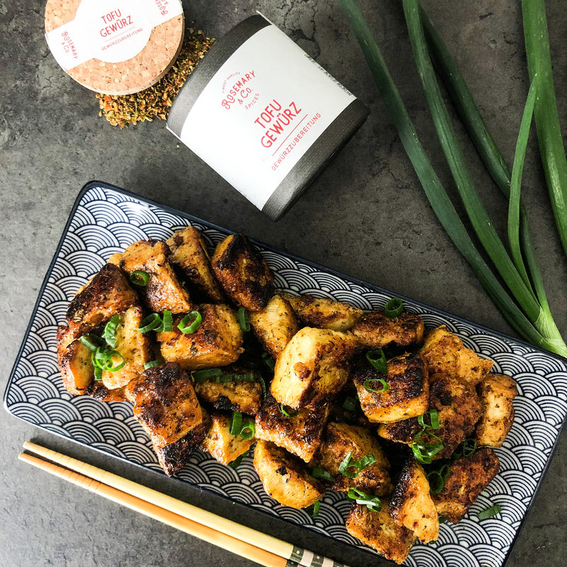 Ein Teller gebratener Tofu mit Tofu-Gewürz und Frühlingszwiebeln daneben, auf einem dunklen Untergrund.