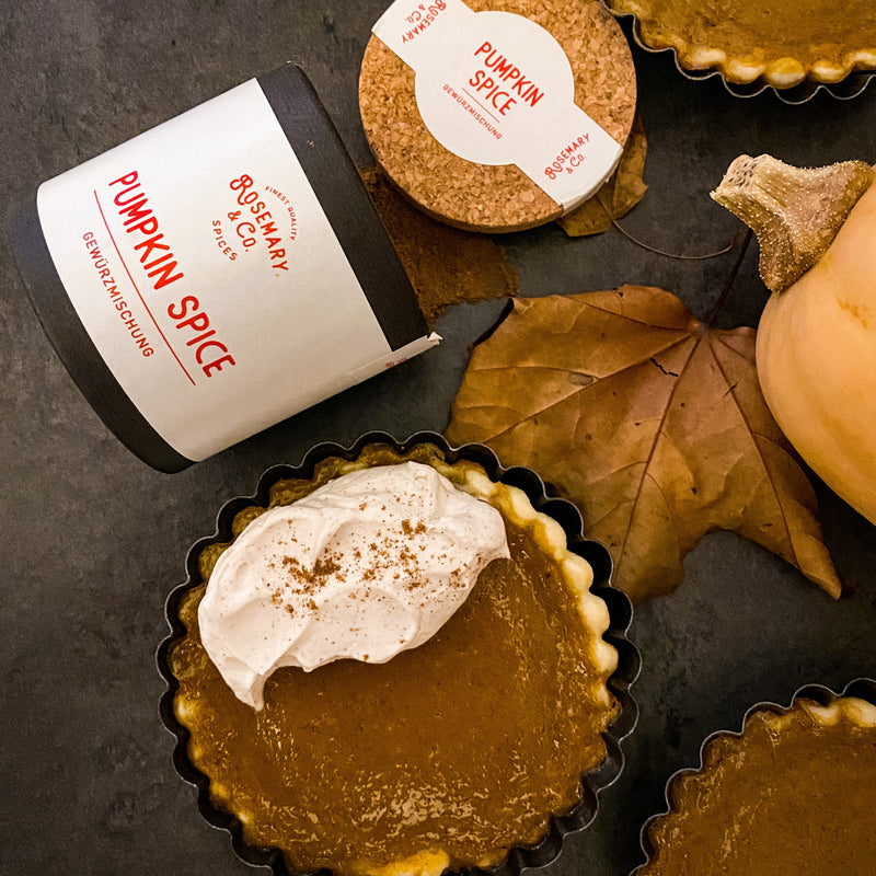 Pappdose mit Pumpkin Spice-Gewürzmischung, Kürbiskuchen mit Sahne und Herbstblättern auf dunklem Hintergrund.