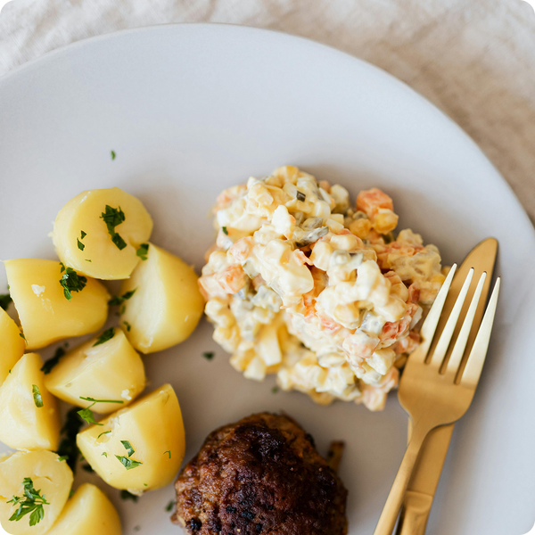 Ein Teller mit Kartoffeln, einem Frikadelle und einem Salat neben einer goldenen Gabel und einem Messer.