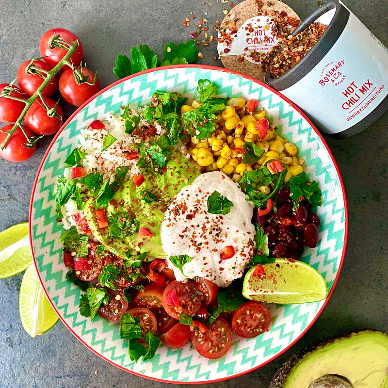 Bunter Salatteller mit Avocado, Bohnen, Mais, Tomaten, Salsa und Limette, daneben eine Dose mit Chili-Mix.