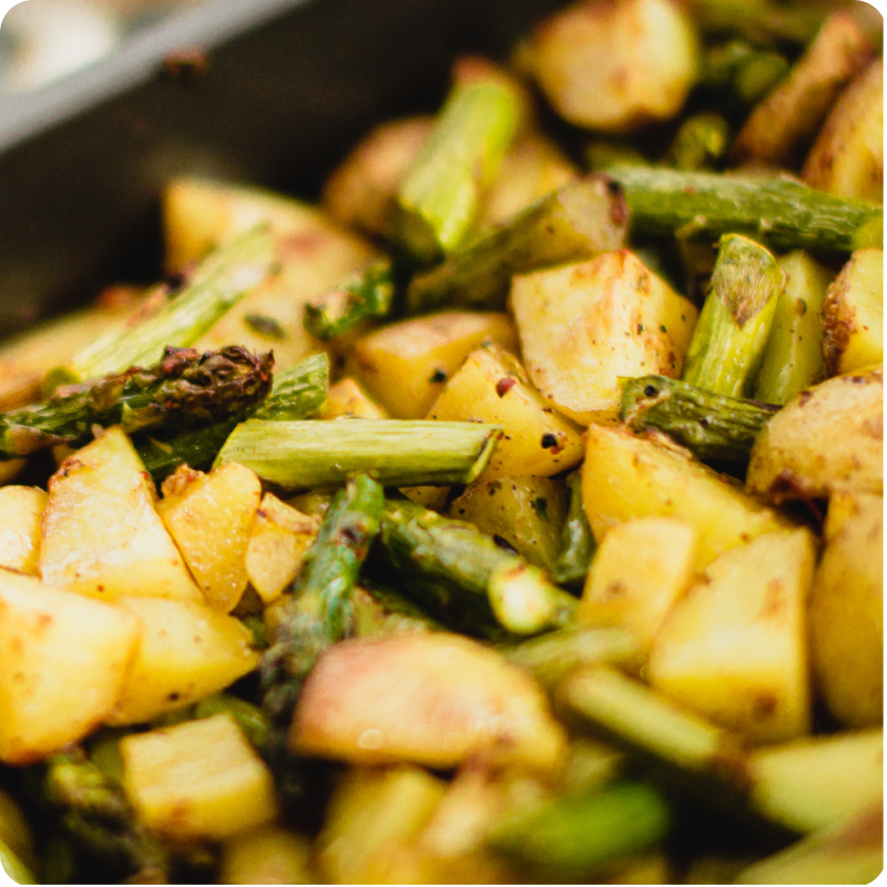 Geröstete Kartoffelwürfel und grüner Spargel in Nahaufnahme, gewürzt und in einer Backform serviert.
