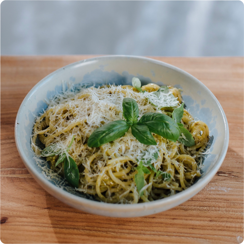 Ein Teller Spaghetti mit Pesto-Sauce, geriebenem Käse und frischem Basilikum auf einem Holztisch.