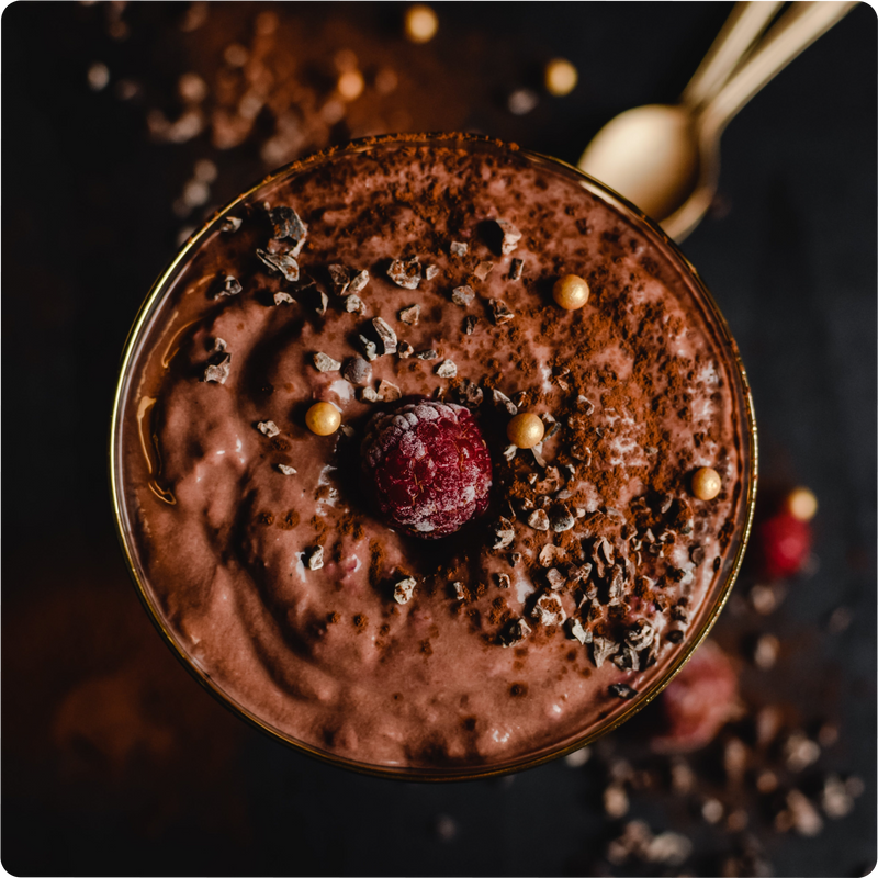 Schokoladenmousse mit Himbeere, Schokoladenstückchen und goldenen Perlen, dekoriert auf dunklem Hintergrund.