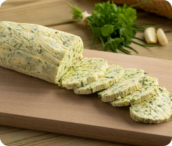 Kräuterbutter auf einem Holzbrett, dahinter Kräuter