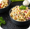 Zwei Schalen mit Nudelsalat, garniert mit Petersilie, auf einem dunklen Untergrund.