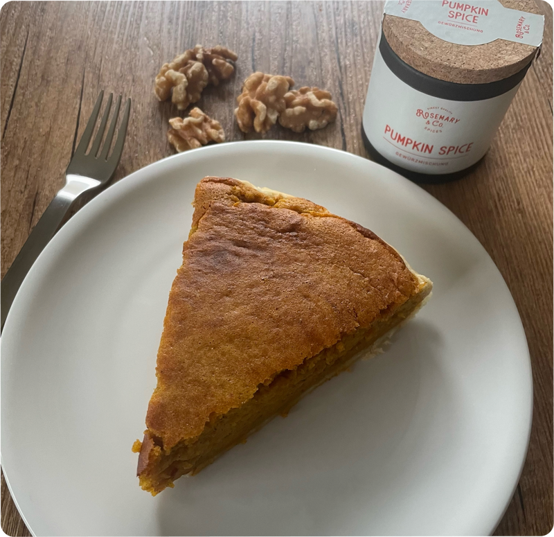 Ein Stück Kuchen auf einem Teller mit Walnüssen und einer Dose Pumpkin Spice auf einem Holztisch.