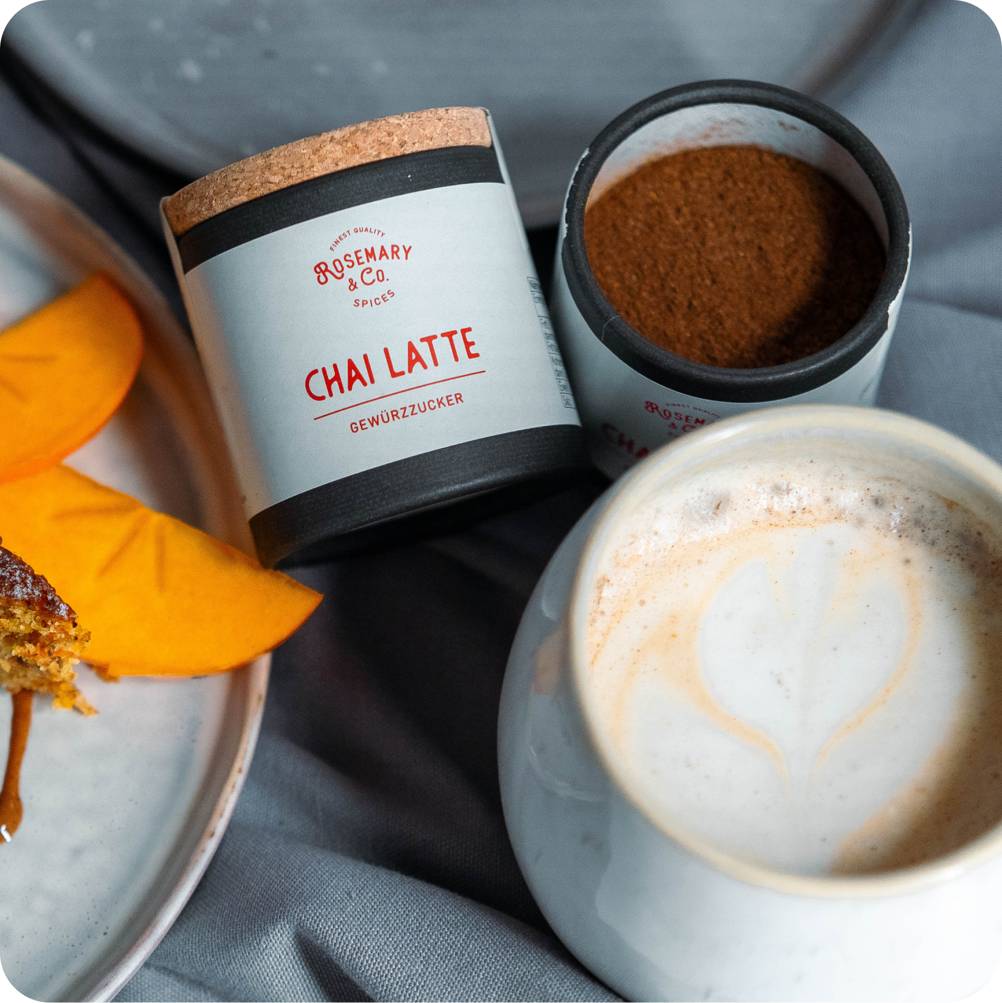 Dose Rosemary & Co. Gewürze Chai Latte geöffnet, Latte und Mangoscheiben auf grauem Tuch