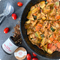 Eine Pfanne mit vegetarischer Pasta, umgeben von Tomaten, Gewürzstreu und einer Pappdose für italienische Gewürze.2