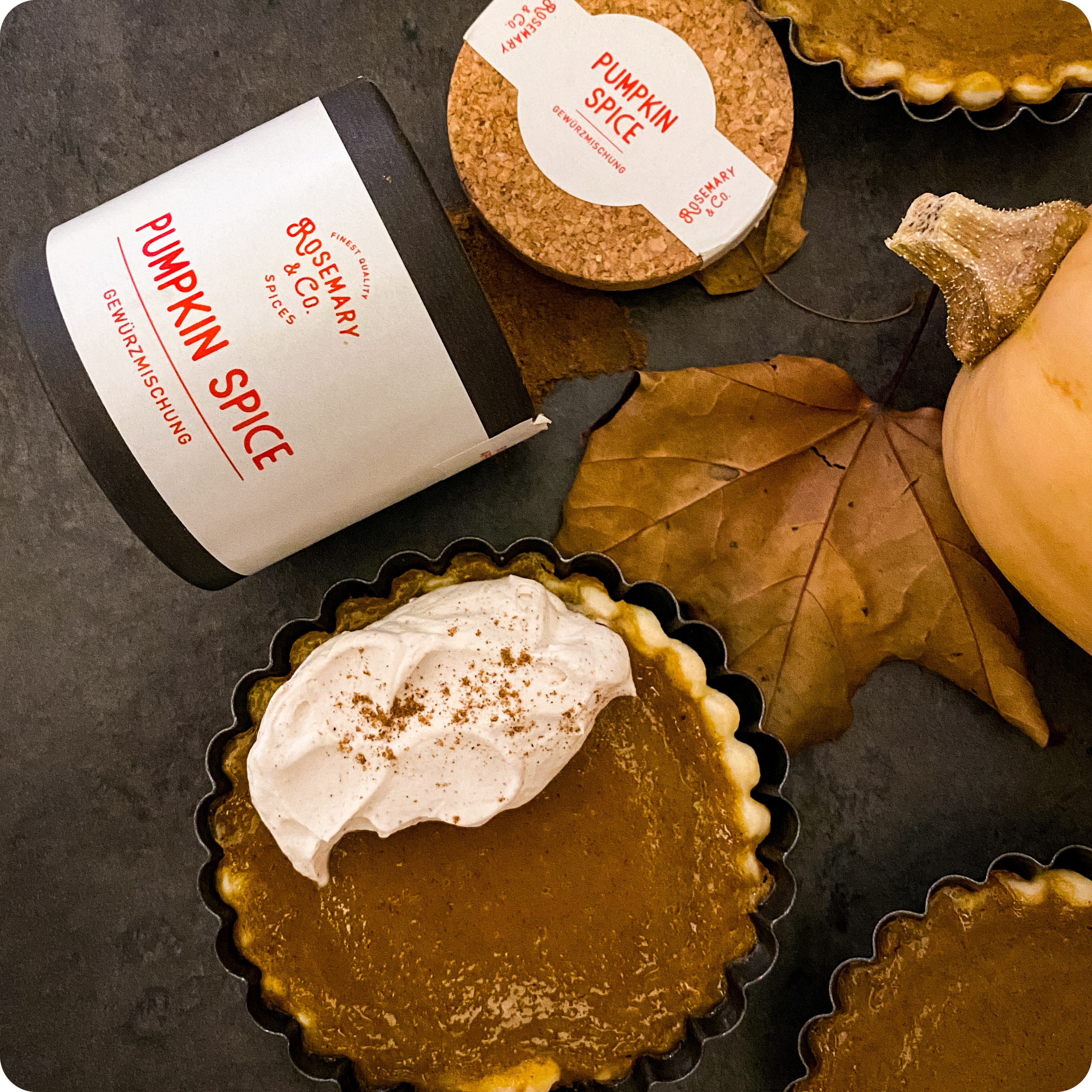 Kleine Kürbistorte mit Sahne neben Dose Rosemary & Co. Pumpkin Spice, kleiner Kürbis und getrockneten Blättern